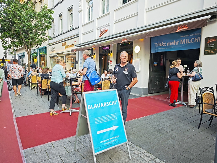Mehrere Personen stehen auf einem roten Teppich der zum Eingang der rheinline weinlounge führt